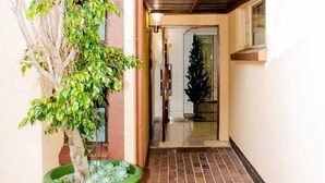 A narrow hallway with a tiled floor, a green planter with a tree, and a Christmas tree in the background. - Erima lodge (Johannesburg)