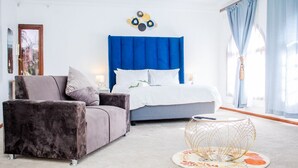 A modern bedroom with a blue headboard, a grey sofa, and a round coffee table. - Erima lodge (Johannesburg)