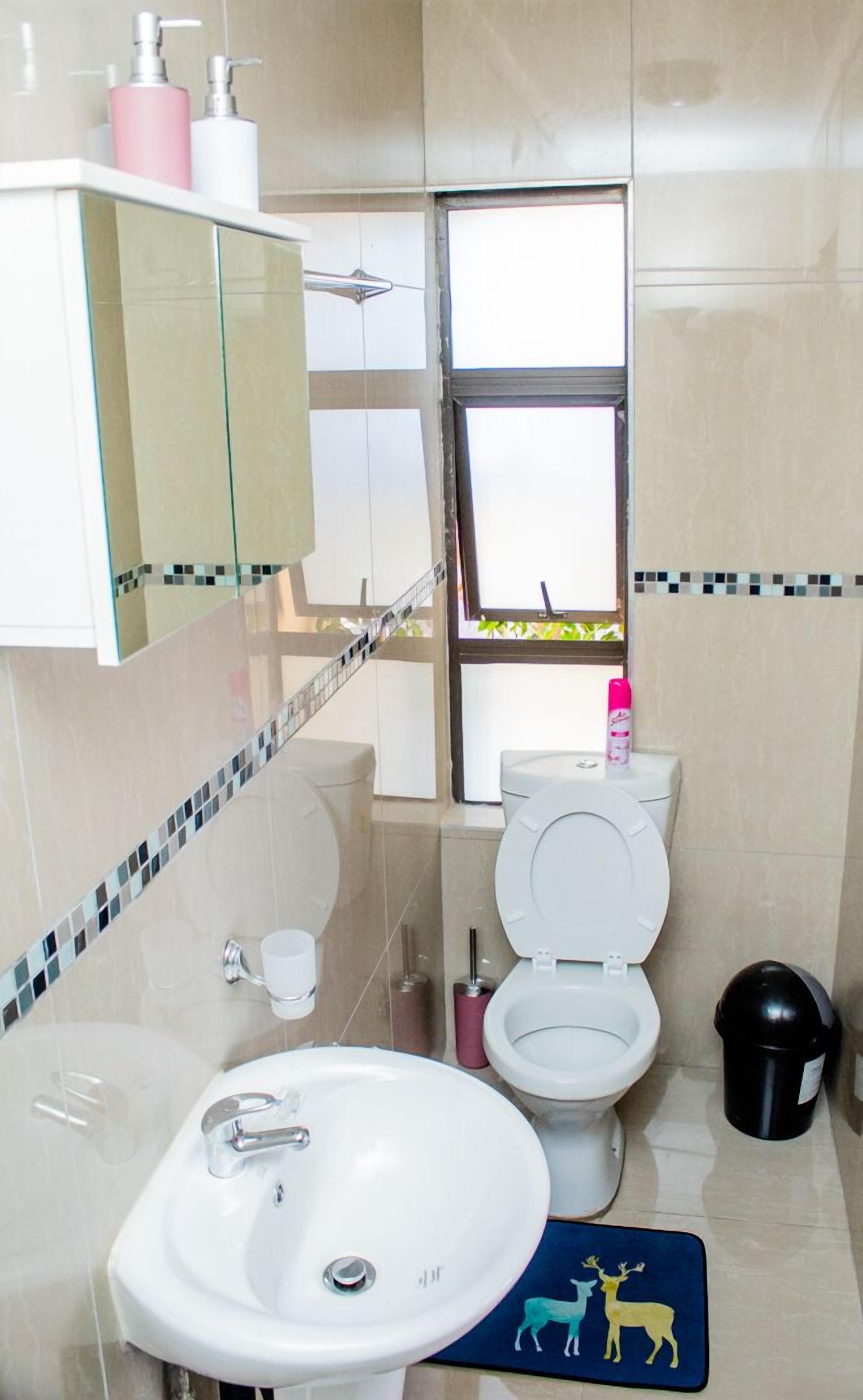 Un baño con lavamanos blanco, inodoro y ventana con vistas a la vegetación.
