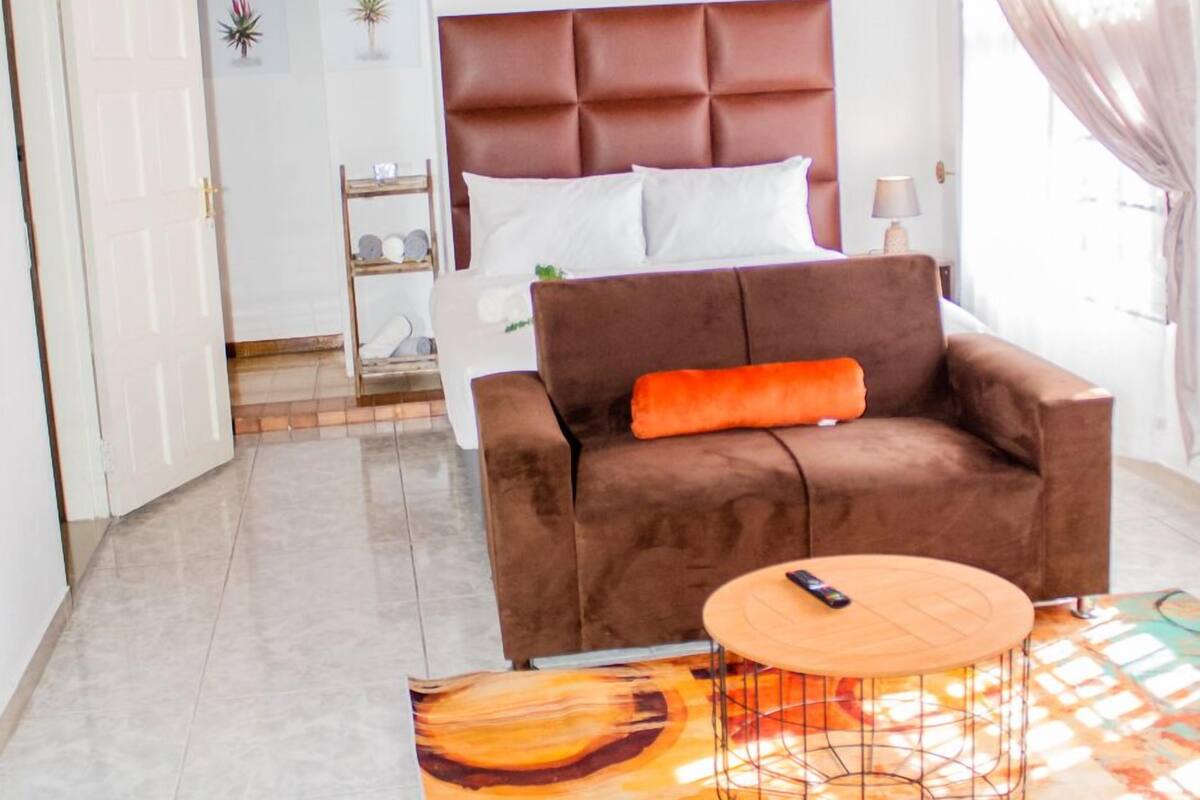 Une chambre à coucher moderne avec un canapé marron, une table basse ronde et un lit doté d’une tête de lit marron.