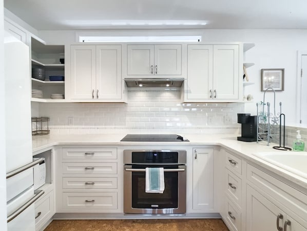 Una cocina moderna con armarios blancos, horno empotrado y cafetera.