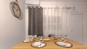 A dining table set with plates, cutlery, and glasses, a clock on the wall, and a window with curtains. - Koukounaria House Holiday Home with Private Pool, Wi-Fi, and Air Conditioning (Zakynthos)