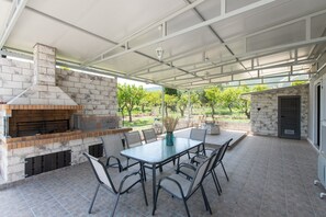 Patio esterno con camino in mattoni, tavolo in vetro e sedie.