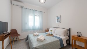 A hotel room with a bed, a desk with a computer, a chair, a TV, and a window with curtains. - Koukounaria House Holiday Home with Private Pool, Wi-Fi, and Air Conditioning (Zakynthos)