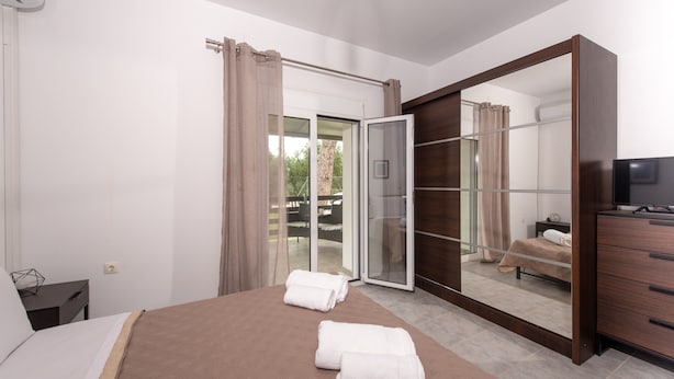 A bedroom with a bed, a wardrobe, a television, and a sliding glass door leading to an outdoor area. - Koukounaria House Holiday Home with Private Pool, Wi-Fi, and Air Conditioning (Zakynthos)
