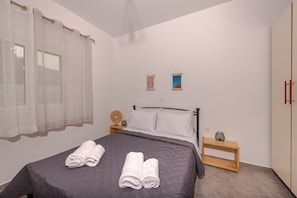 Une chambre à coucher comprenant un lit, deux tables de chevet, une commode, une fenêtre avec des rideaux et deux tableaux accrochés au mur.