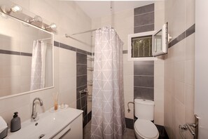 Un bagno con tenda da doccia, un water, un lavandino con dispenser di sapone, uno specchio e una finestra.