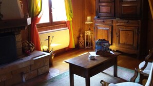A cozy cabin interior with a fireplace, wooden furniture, and a window with curtains.