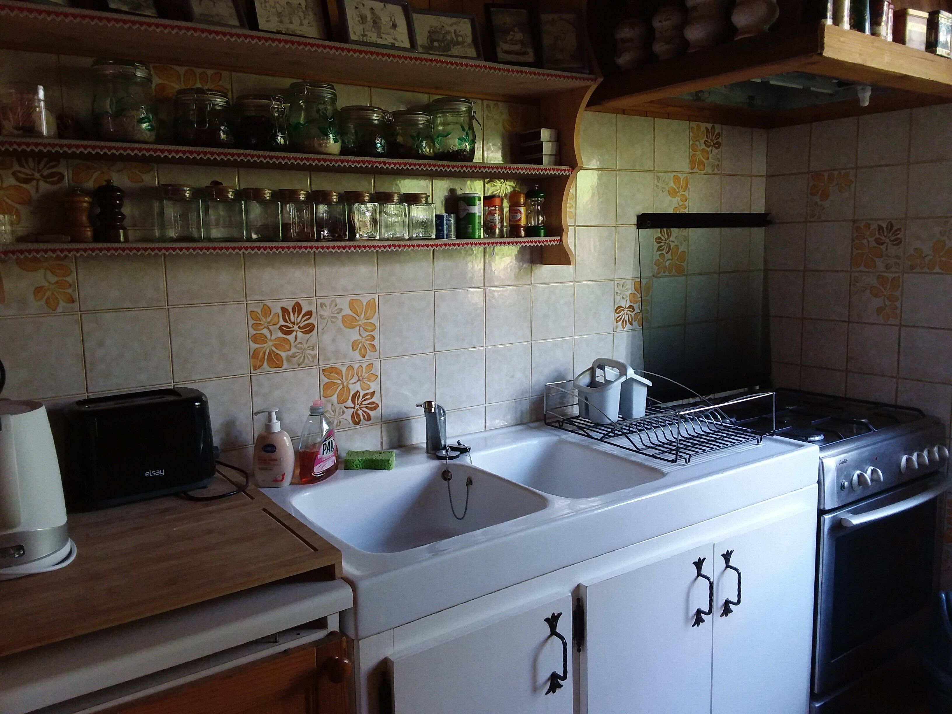 Une cuisine équipée d’un évier, d’une cuisinière et d’étagères où sont rangés des bocaux et des bouteilles.