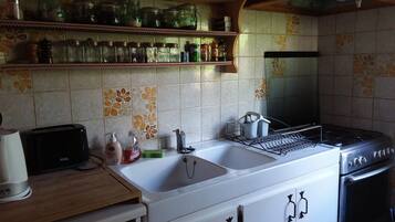 Une cuisine équipée d’un évier, d’une cuisinière et d’étagères où sont rangés des bocaux et des bouteilles.