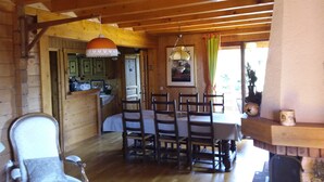 A wooden interior with a dining table, chairs, a kitchen area, and a fireplace.