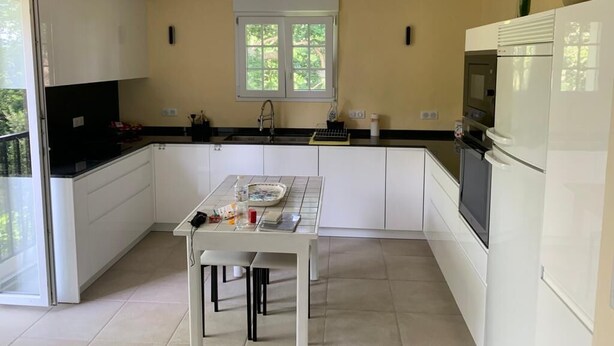 Una cocina moderna con armarios blancos, encimera negra, ventana con vistas y un refrigerador.