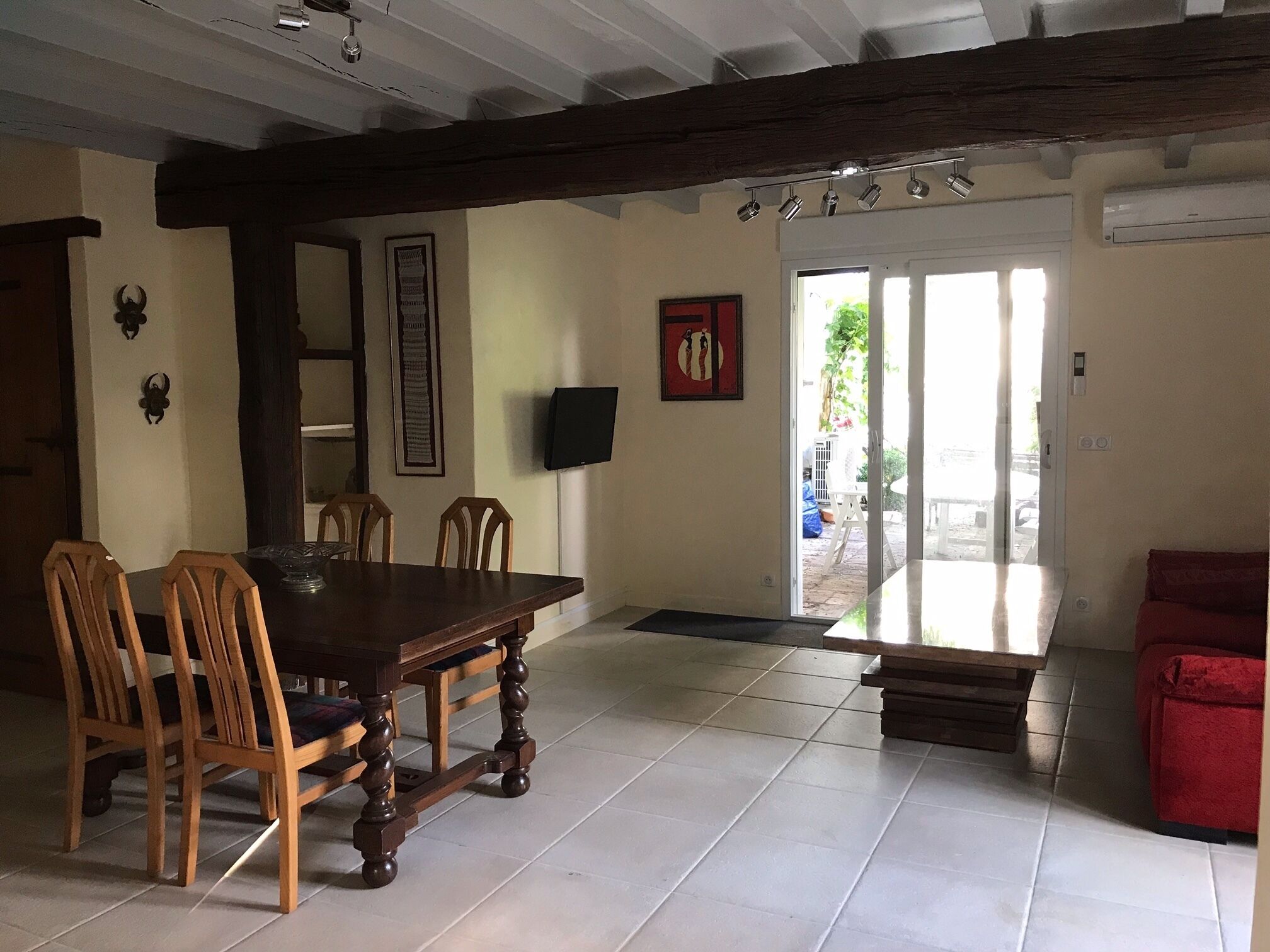 Un comedor con una mesa y sillas de madera, un televisor montado en la pared y un sofá rojo en la esquina.