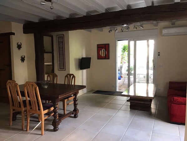 A dining area with a wooden table and chairs, a television mounted on the wall, and a red sofa in the corner.