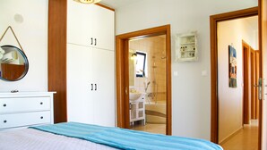 A bedroom with a bed, a dresser, a mirror, and a bathroom visible through an open door. - Villa Stefania with Pool (Rethymno)