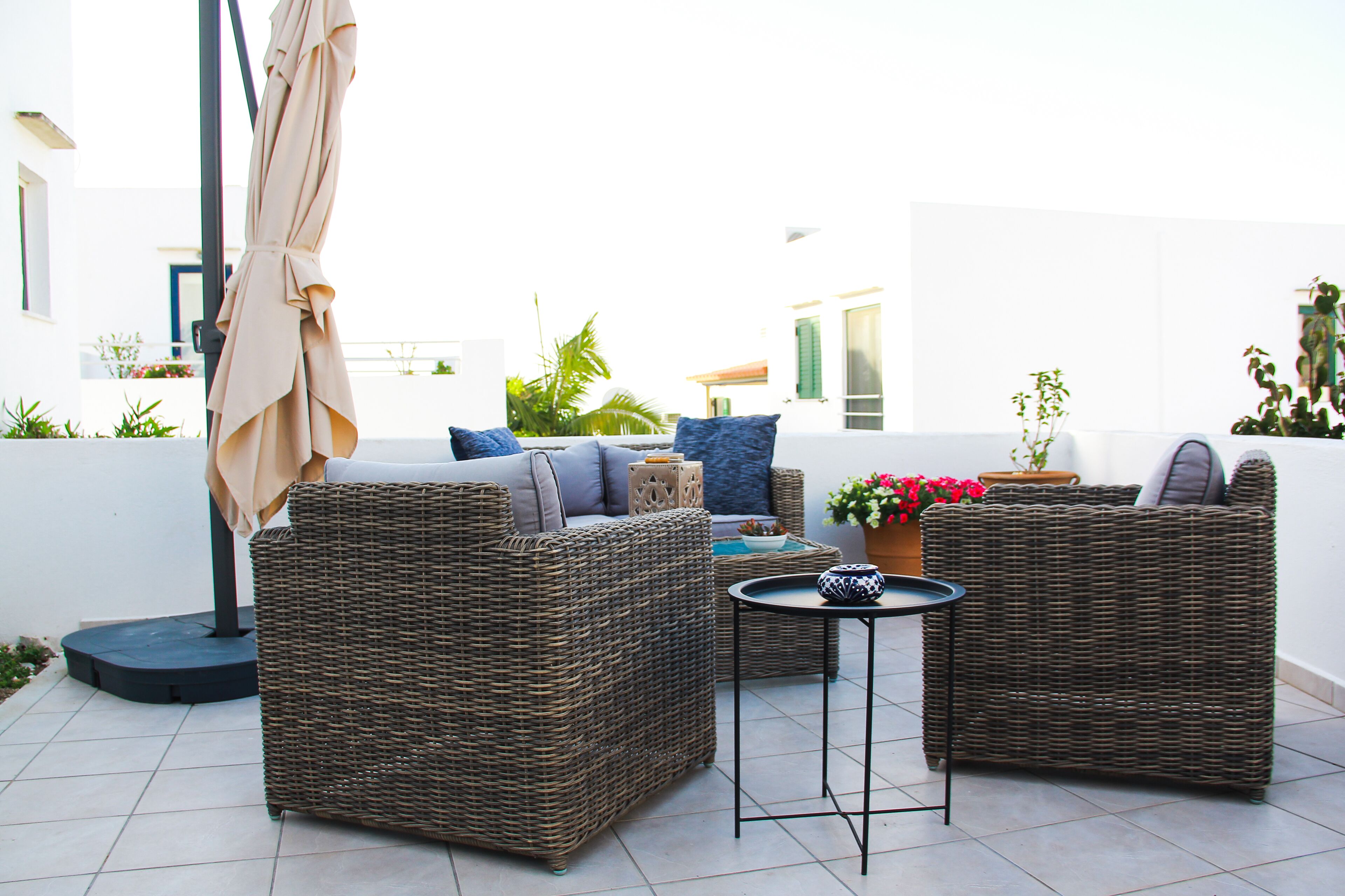 A wicker sofa set with cushions, a small round table, and a potted plant on a tiled patio.