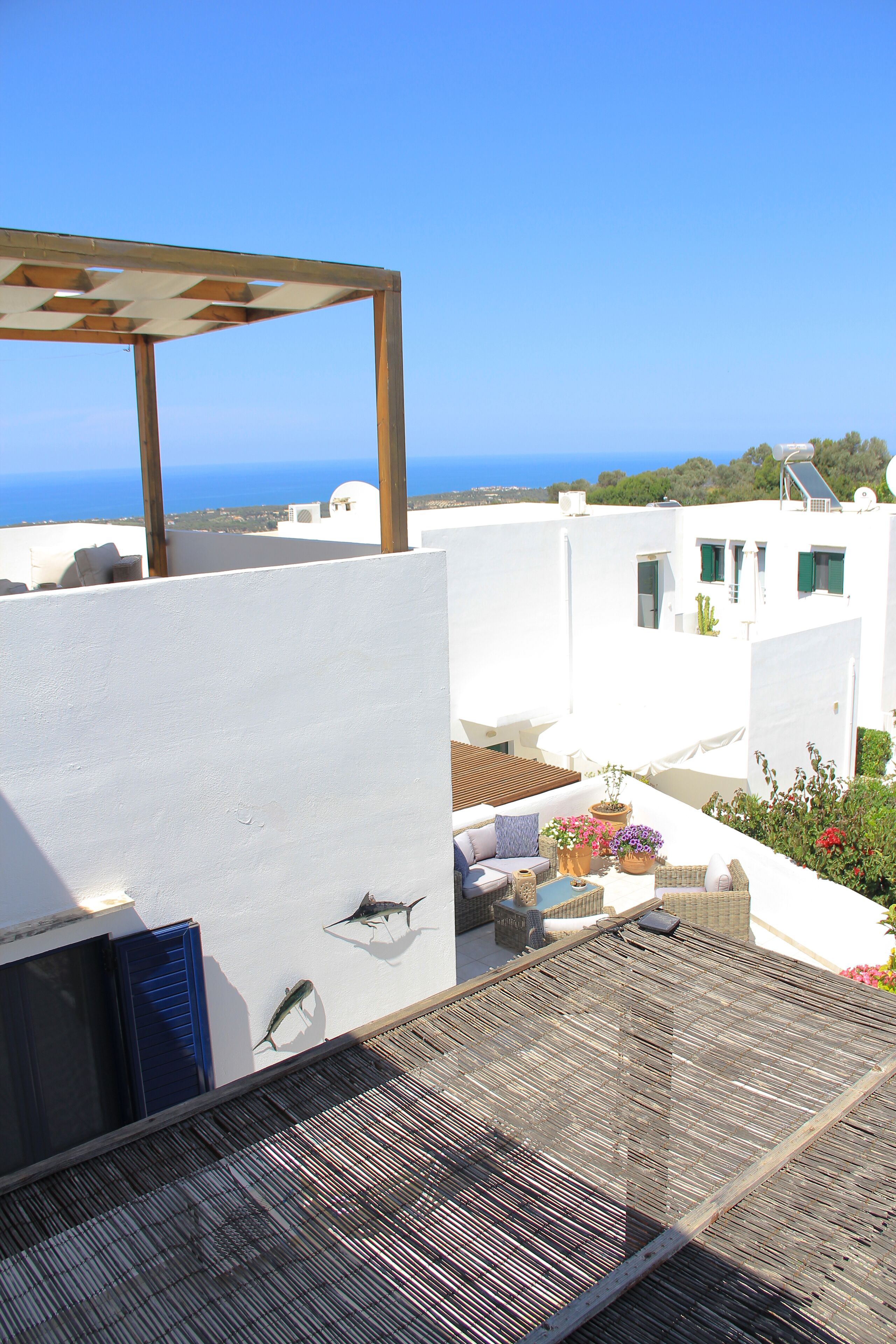 Terraço no telhado com vista para o mar, edifícios brancos e alguns vasos com plantas.
