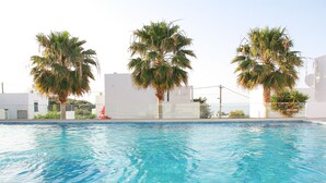 A swimming pool with clear blue water, surrounded by white buildings and palm trees. - Villa Stefania with Pool (Rethymno)