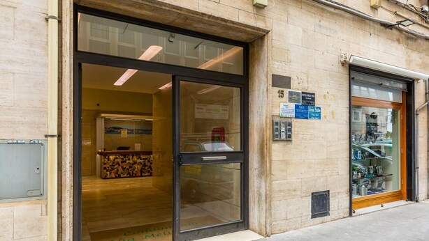 A hotel entrance with a reception desk, a glass door, and a visible sign for room rates. - La Dimora Dell Avvocato - Appartamento (Naples)