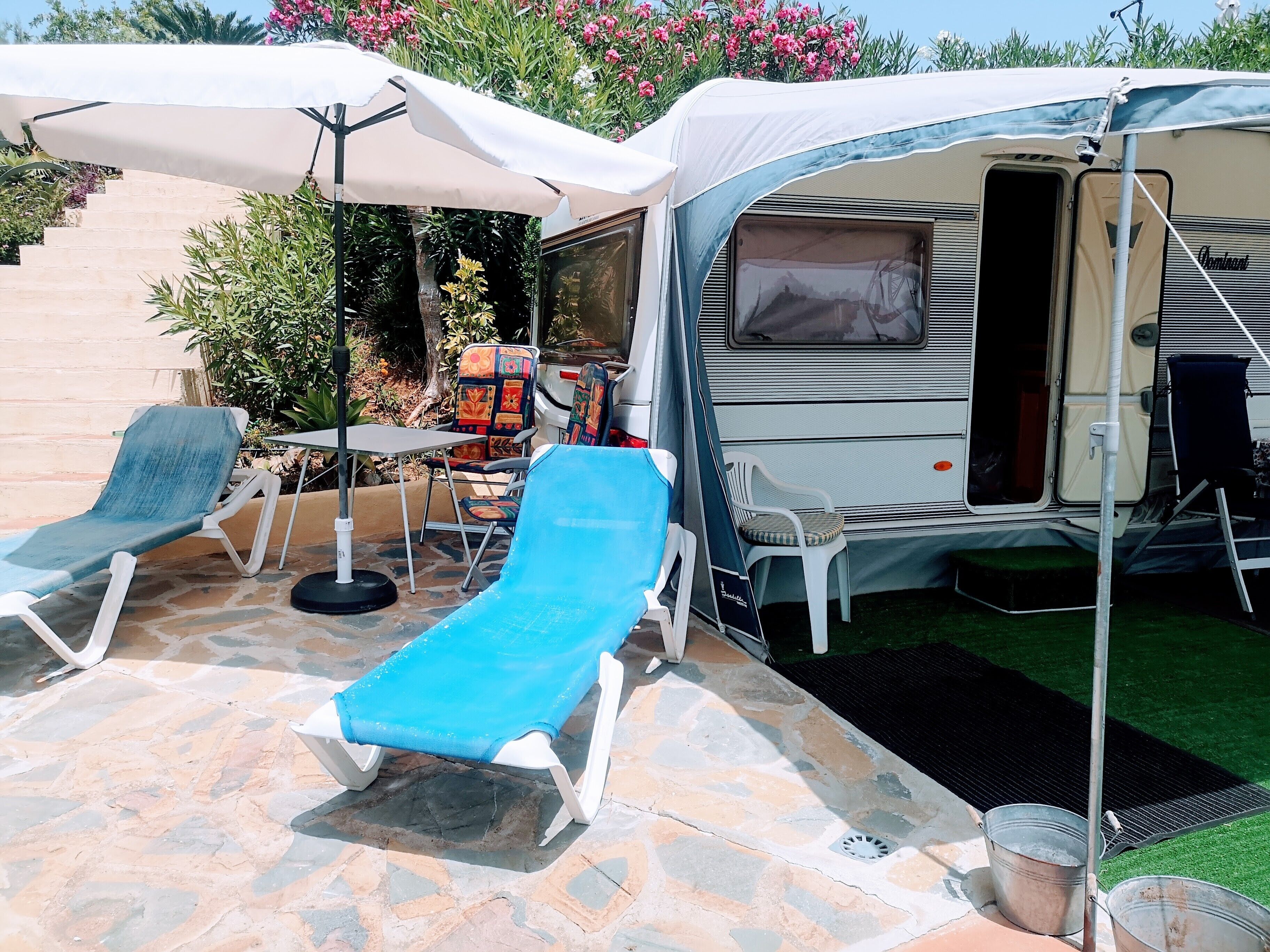 Una caravana con un porche cubierto, mobiliario exterior y una pequeña mesa.