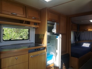 Une cuisine compacte pour camping-car, dotée d’une fenêtre, d’une cuisinière et d’un réfrigérateur.