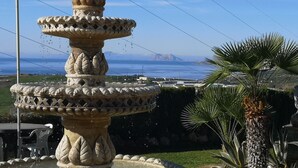 Una font de pedra amb disseny per terrasses, envoltada de vegetació i amb vista al mar.