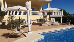 A poolside area with lounge chairs and umbrellas, a tiled pool, and a building with a balcony. - Studio Apartment "Roca Penthouse"no kids under 10 year, with Sea View, Shared Pool & Wi-Fi (Estepona)