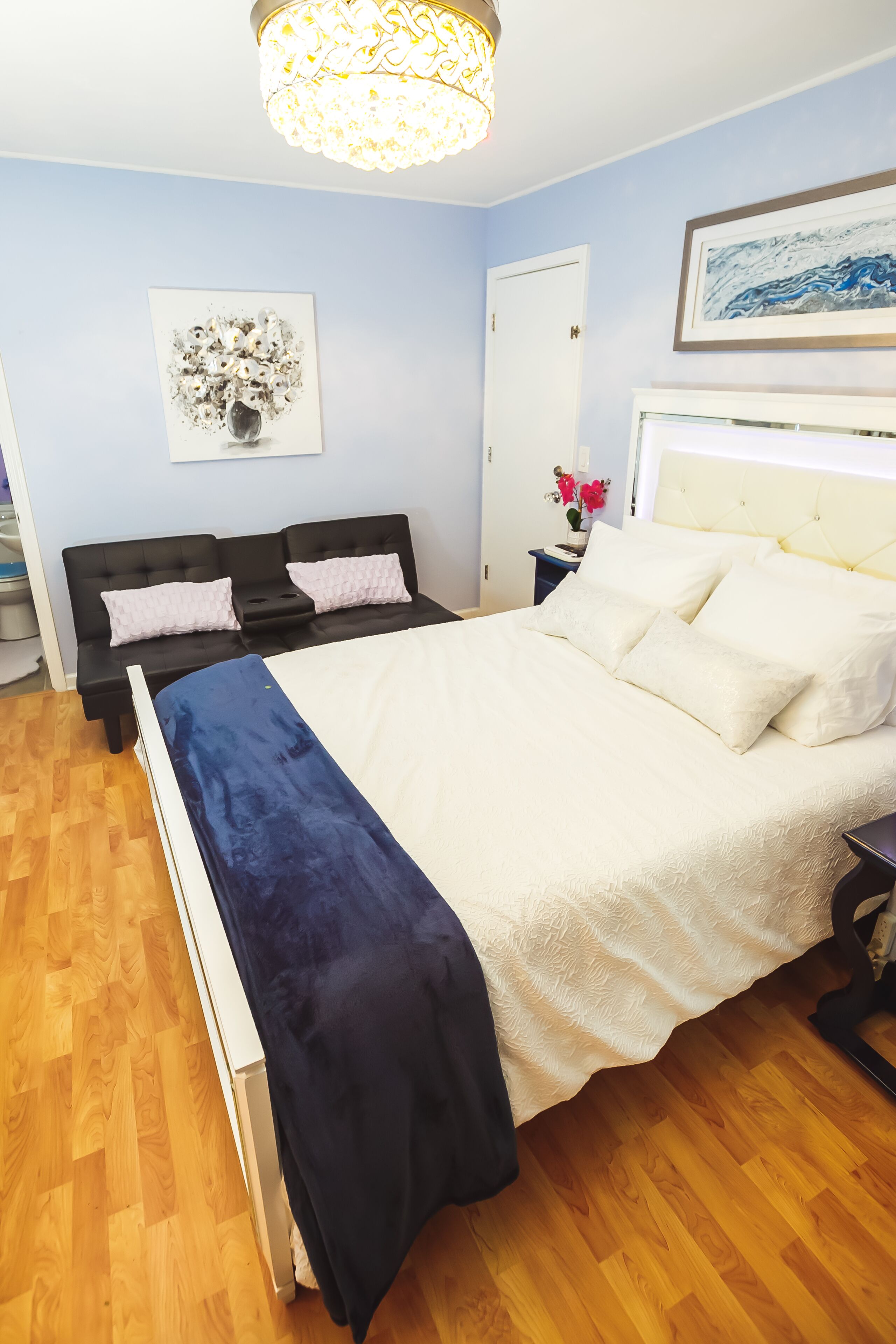 A bedroom with a bed, a nightstand, a wall-mounted lamp, and a door.