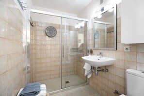 Un baño con cabina de ducha de vidrio, lavamanos e inodoro.