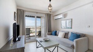 Ein modernes Wohnzimmer mit einer Couch, einem Couchtisch, einem Fernseher und einem Balkon mit Vorhängen.