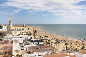 Un paisaje urbano costero con una iglesia destacada, una playa con sombrillas y edificios residenciales.