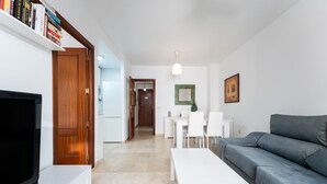 A living room with a TV, white furniture, a grey sofa, and a bookshelf. - 'City in Fuengirola Centro' Apartment with Balcony and Wi-Fi (Fuengirola)