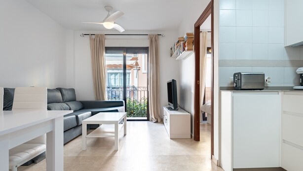 A modern living room with a sofa, a coffee table, a TV, and a kitchen area with a microwave. - 'City in Fuengirola Centro' Apartment with Balcony and Wi-Fi (Fuengirola)