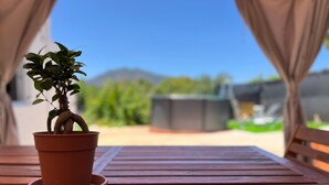Ein terrakotta-Topf mit Pflanze auf einem Holztisch mit Blick auf eine grüne Landschaft und Berge im Hintergrund.