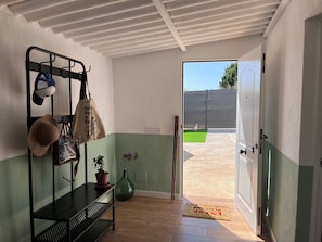 A room with a bench, hats, a tote bag, a potted plant, and a door leading outside.