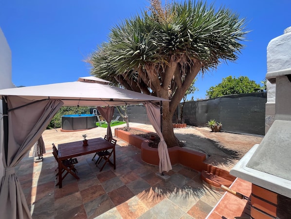 A patio with a table and chairs, a covered area, a tree, and a barbecue grill.