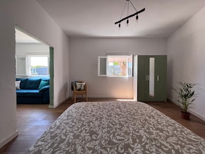 A bedroom with a bed, a window, a wardrobe, a chair, and a view of an outdoor area.