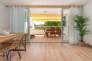 A modern interior with a wooden dining table, wicker chairs, a potted plant, and a balcony with a yellow-striped awning. - Holiday Apartment 'Brava Beach' with Shared Pool, Private Terrace & Wi-Fi (platja d'aro)