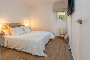 A bedroom with a bed, bedside lamps, a window with a view, a radiator, and a television mounted on the wall.