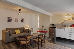 Ein modernes Wohnzimmer mit einer Couch, Esstisch, Stühlen und einer Küchenzeile mit Spüle und Schränken.