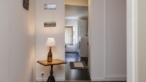 Um corredor com luminária, garrafa e uma mesinha. Quadros emoldurados na parede.