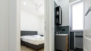 A modern bedroom with a bed, a ceiling fan, a bathroom with a sink and mirror, and a radiator. - Via Niccol Tommaseo 4 - Appartamento 4 (Naples)