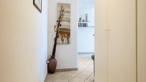 Um corredor com um vaso grande e uma pintura na parede, que leva a um quarto com uma porta.