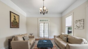 Un soggiorno con due divani color beige, un poggiapiedi blu, un lampadario e un tappeto decorato.