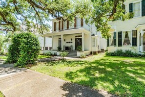 A two-story house with a front porch, a small front yard, and a large tree.
