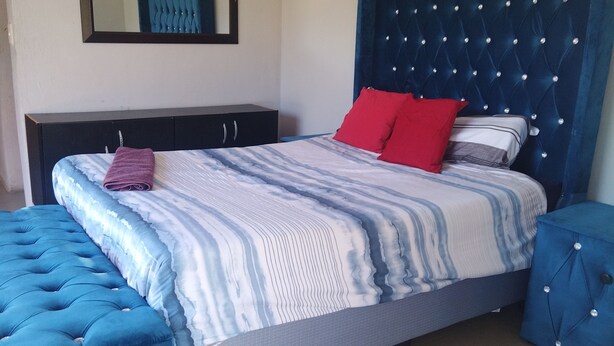 A bedroom with a bed, a nightstand, a dresser, a mirror, and a blue upholstered bench. - Moholoholo lodge  (Bushbuckridge)