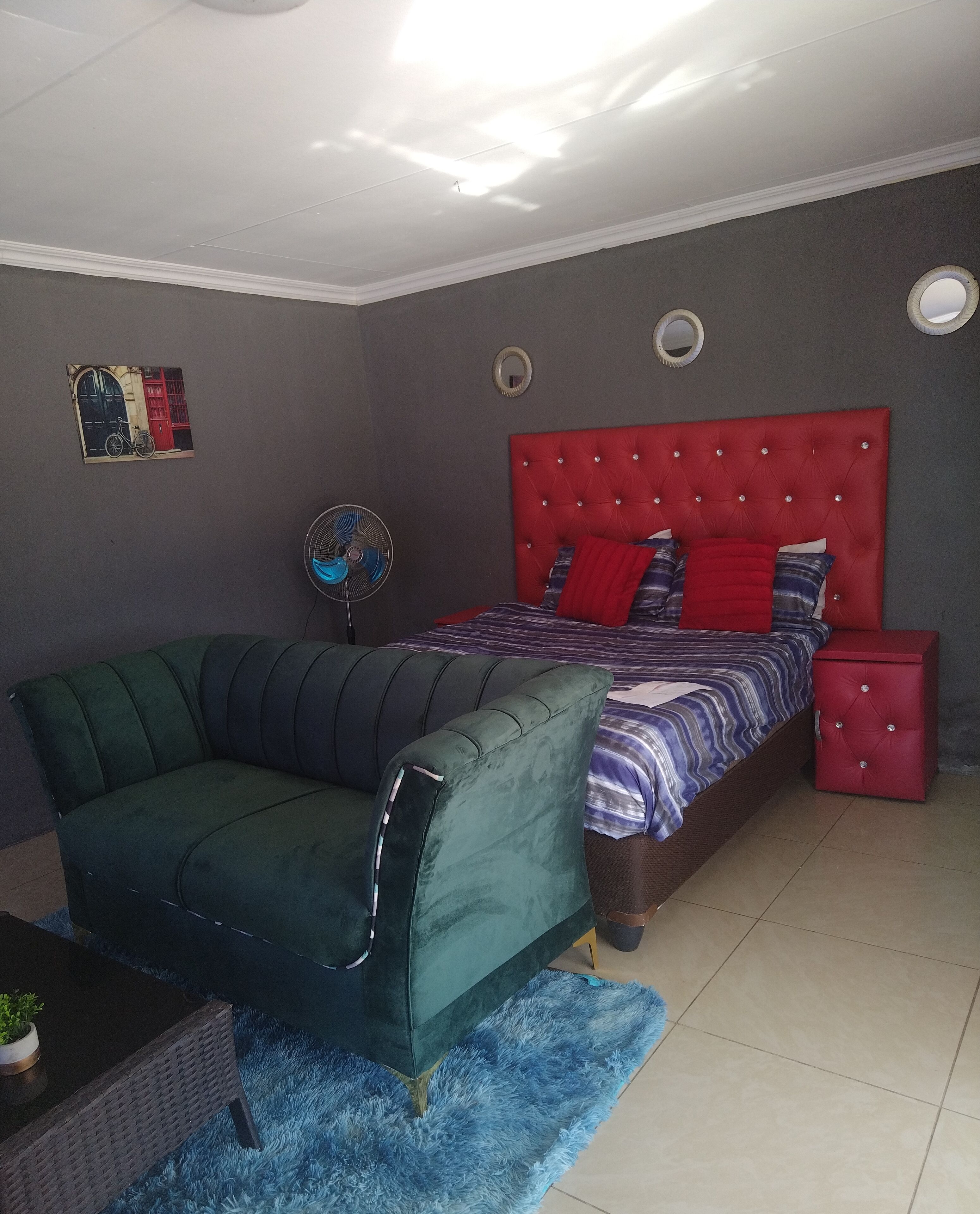 A bedroom with a bed, a green sofa, a red cabinet, and a wall-mounted fan.
