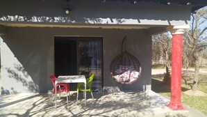 A small building with a green roof, a door, and a window. There is a table with chairs and a hanging chair outside. - Moholoholo lodge  (Bushbuckridge)