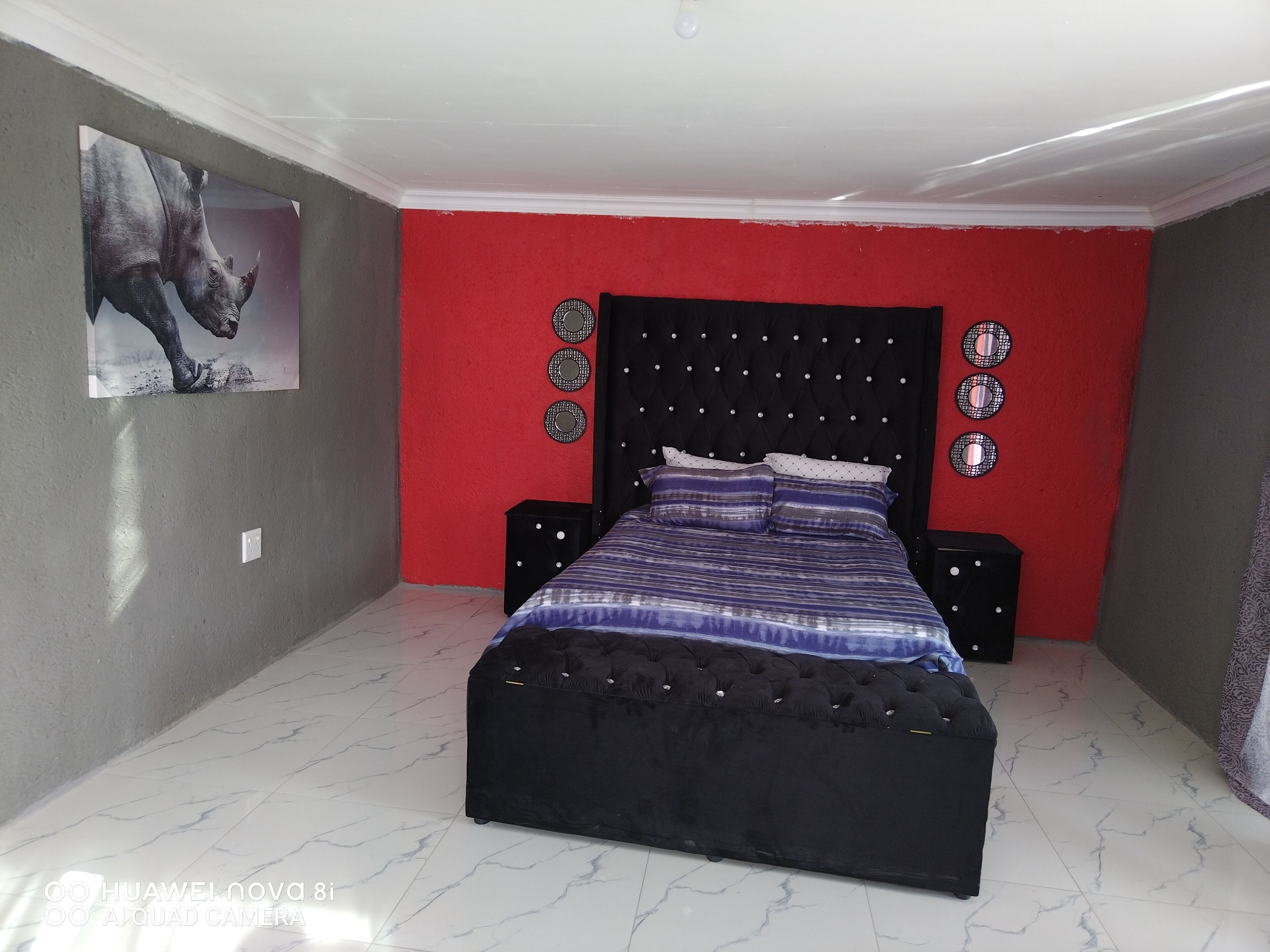 Une chambre avec un lit noir, des murs rouges et un sol en marbre.