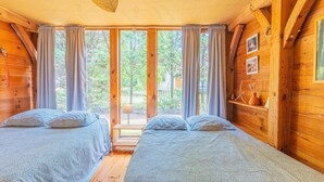A cabin with two beds, a window with curtains, and a wooden interior.